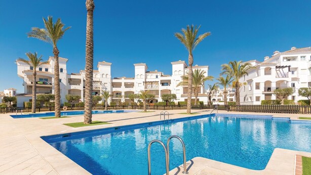 A swimming pool with two ladders, surrounded by palm trees and white buildings with balconies. - Gorgeous apartment in Roldán with WiFi (Roldán)