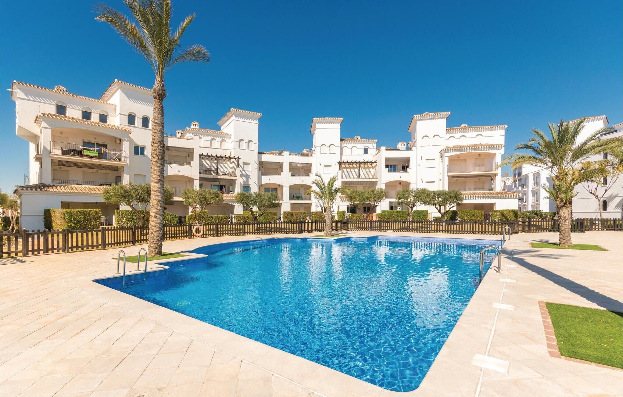 Una piscina rodeada por un edificio blanco con balcones y palmeras.