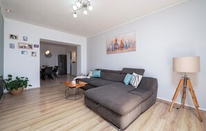 A modern living room with a grey sofa, a wooden coffee table, and a floor lamp. There is a dining area in the background with a black refrigerator and a dining table. - Amazing apartment in Rabac (Rabac)