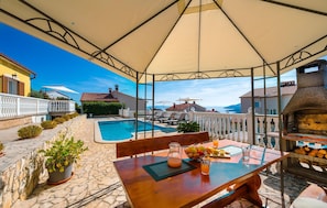 Uma área à beira da piscina com uma mesa posta para dois, churrasqueira e vista para o mar.