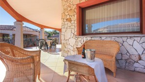 An outdoor patio with wicker furniture, a table with a bottle and a metal container, and a stone wall.