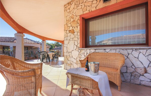 Une terrasse extérieure avec des meubles en osier, une table avec une bouteille et un récipient en métal, et un mur en pierre.