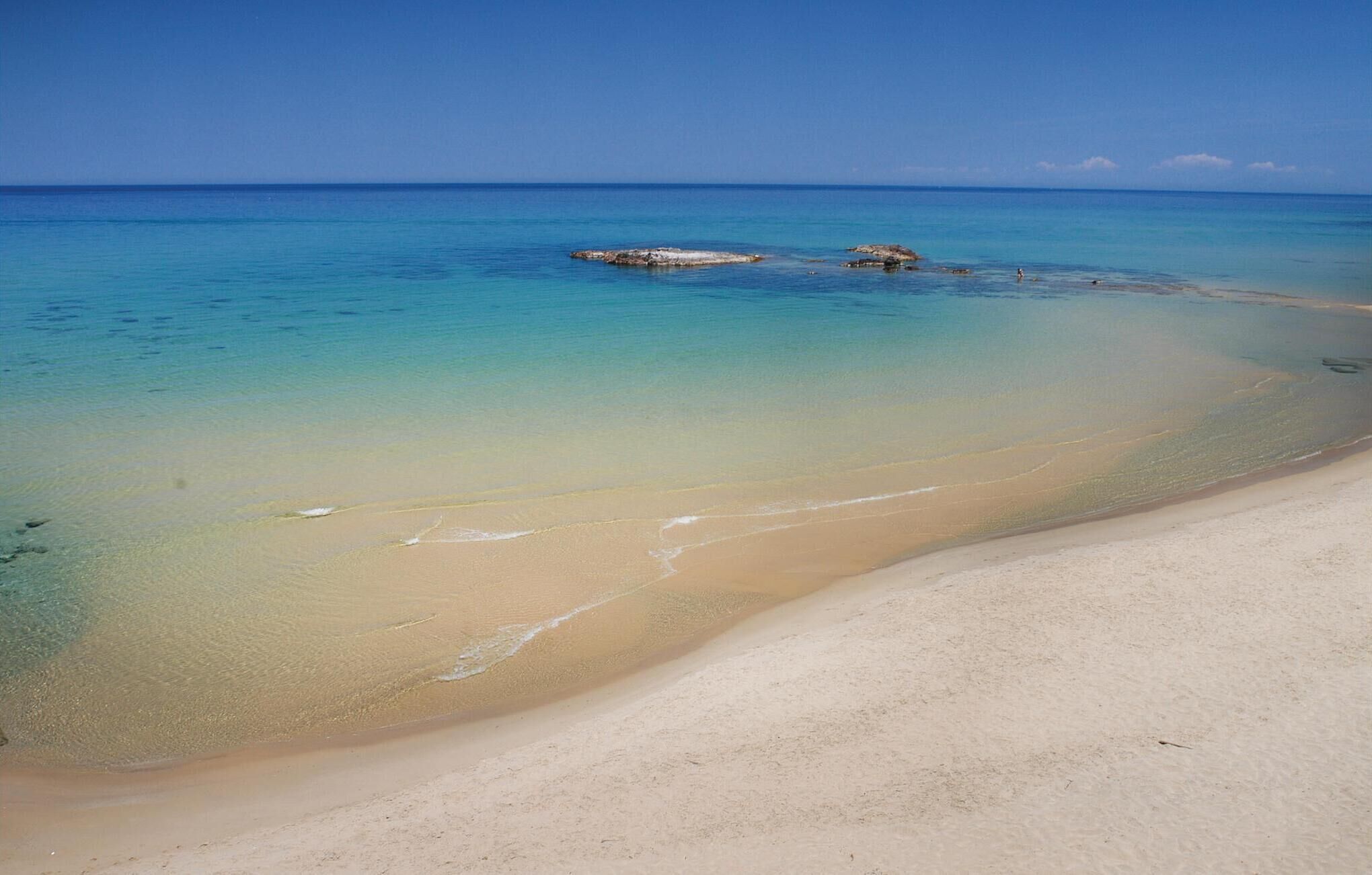 A beach with clear water, sandy shore, and a rocky outcrop.