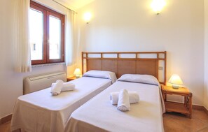 Habitación de hotel con dos camas individuales, una ventana con cortinas, un calentador de pared y lámparas de noche.