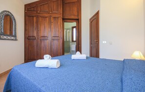 A bedroom with a large wooden wardrobe, a bed with blue bedding, and a bathroom visible through an open door. - 3 bedroom lovely home in Costa Rei -CA- (Costa Rei -CA-)