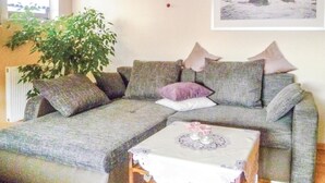 A living room with a grey sofa, a small table with a lace tablecloth, and a large green plant. - Beautiful apartment in Schönecken (Schönecken)