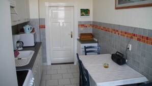 Une cuisine de taille réduite avec une porte blanche, une horloge, une radio et une petite table recouverte d’une nappe.