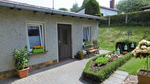 Une maison avec une cour avant pavée, un banc et des plantes en pot.