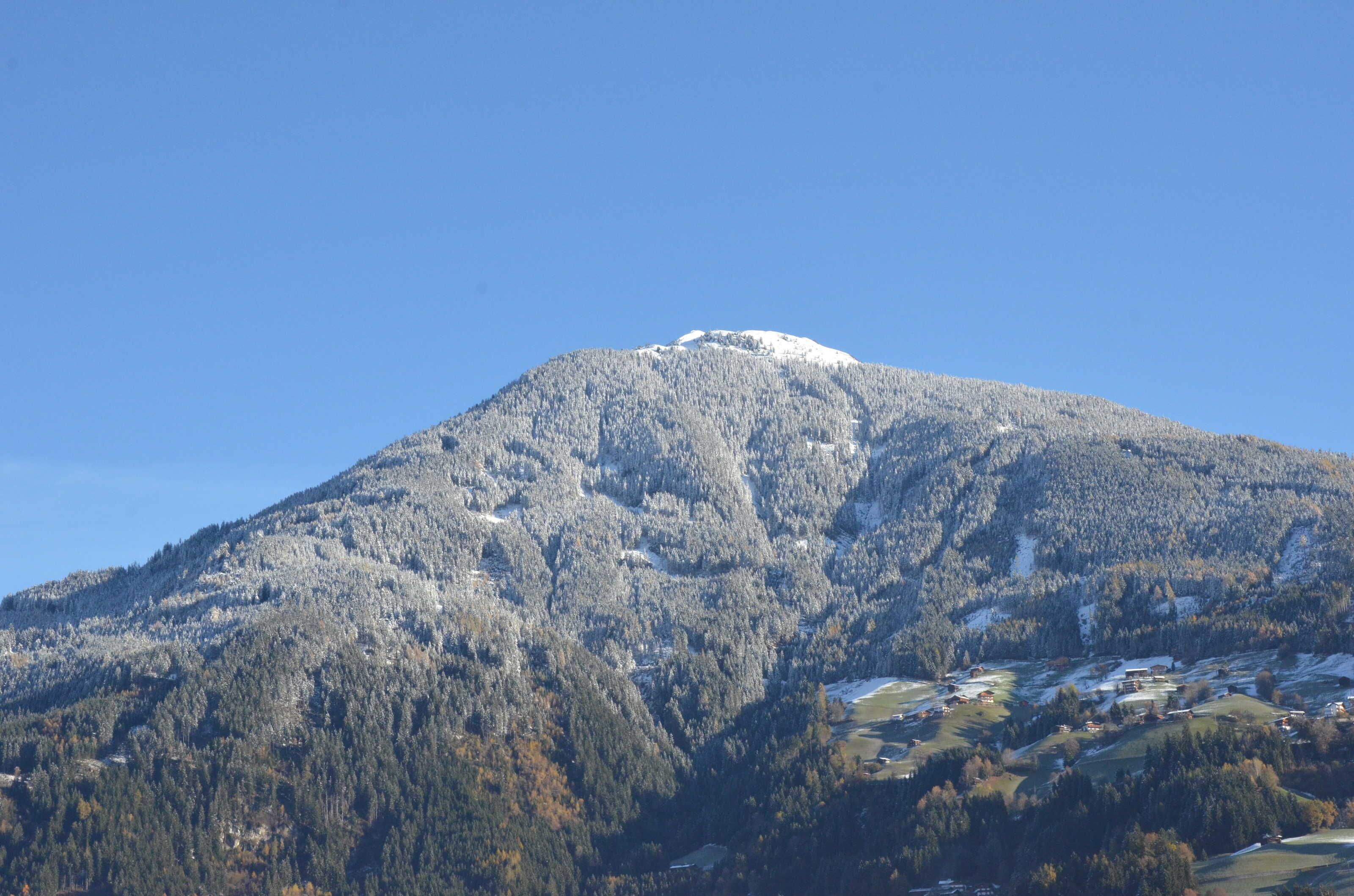 Une montagne dont le sommet est coiffé de neige, dont les flancs sont couverts de forêts et au pied de laquelle se trouvent quelques bâtiments dispersés.