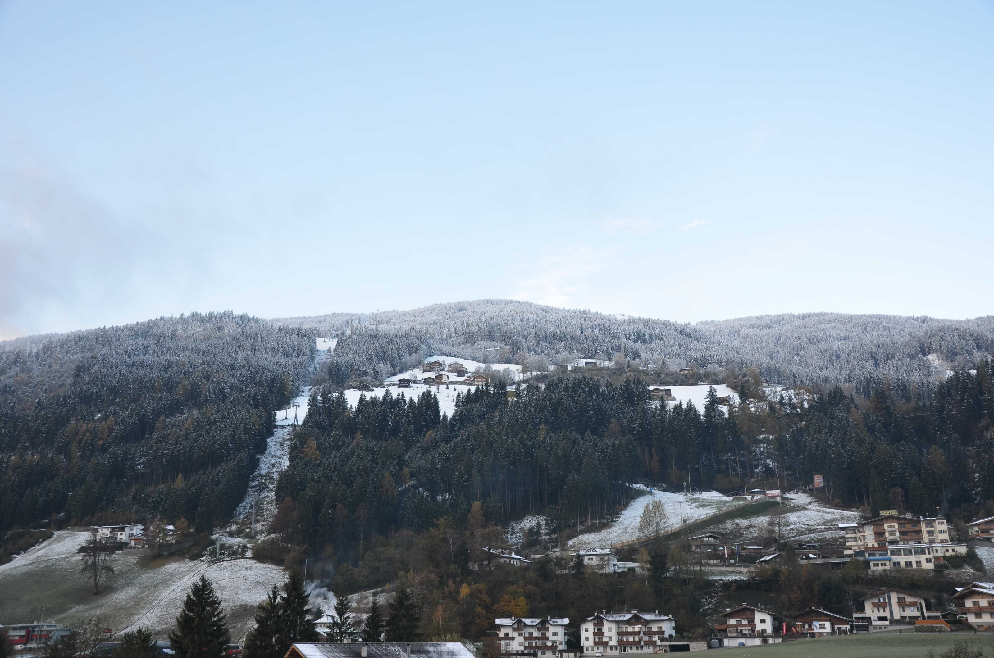 Ein Bergdorf mit Häusern an einem Hang, eine Skipiste und ein klarer Himmel.