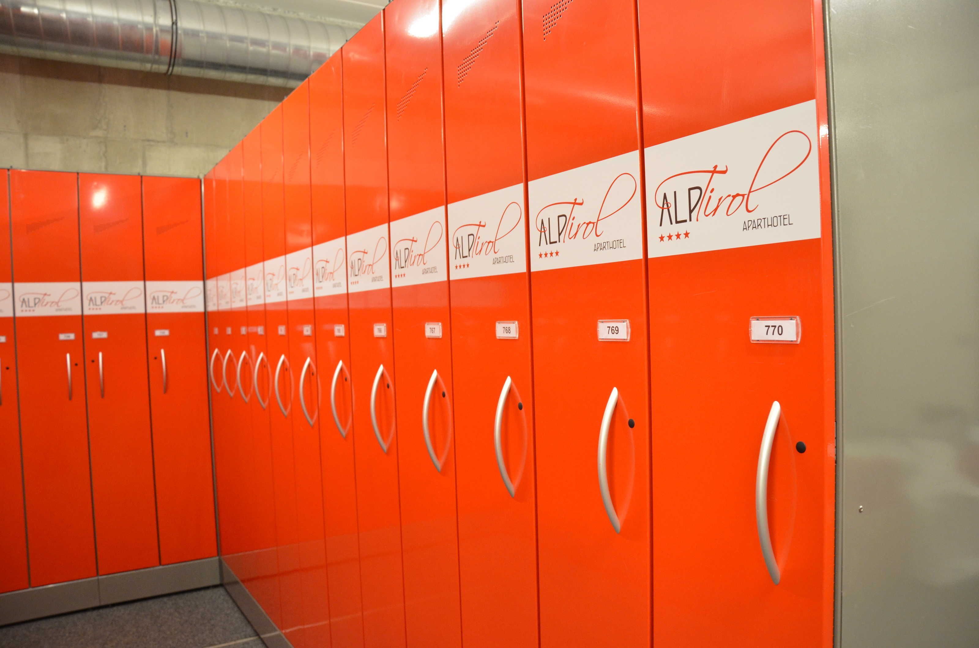 Een rij oranje lockers met het 'AlpTril'-logo en zichtbare kamer nummers.