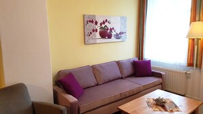 A room with a brown sofa, a small table, and a painting of flowers on the wall.