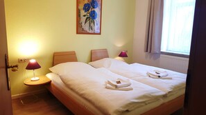 A double bed with white linens, two pillows, a nightstand with a lamp, and a painting on the wall.