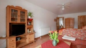 A room with a wooden cabinet, a television, a red sofa, a ceiling fan, and a plant. - Apartment 3 - Apartments Family Mall (Benz)