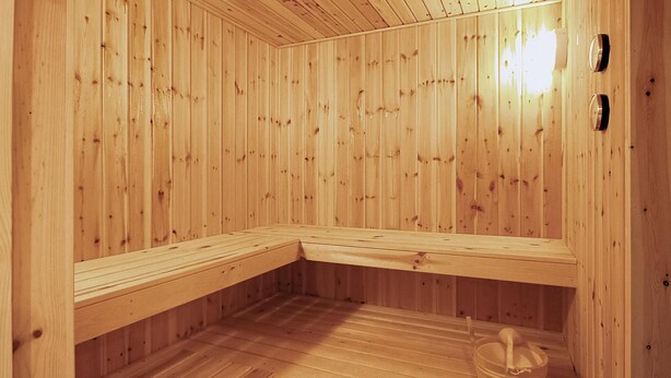 Un sauna avec des murs et des bancs en bois, un banc muni d’un seau et d’une brosse, et un luminaire fixé au mur.