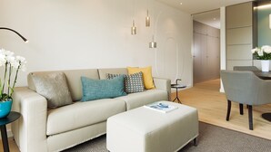 A modern living room with a beige sofa, a matching ottoman, and a dining area with a grey chair. - K6 from A&M - K6, Germany (Kampen (Sylt))
