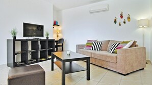Ein modernes Wohnzimmer mit Flachbildfernseher, einer Couch, einem Couchtisch und einem Bücherregal.