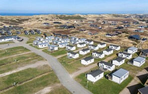 An aerial view of a caravan park with compact, white mobile homes arranged in rows, surrounded by grassy fields and dunes, with a clear view of the sea in the background. - Stunning home in Hvide Sande with WiFi (Hvide Sande)