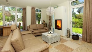 Ein Wohnzimmer mit einer Couch, einem Couchtisch, einem Kamin und großen Fenstern.