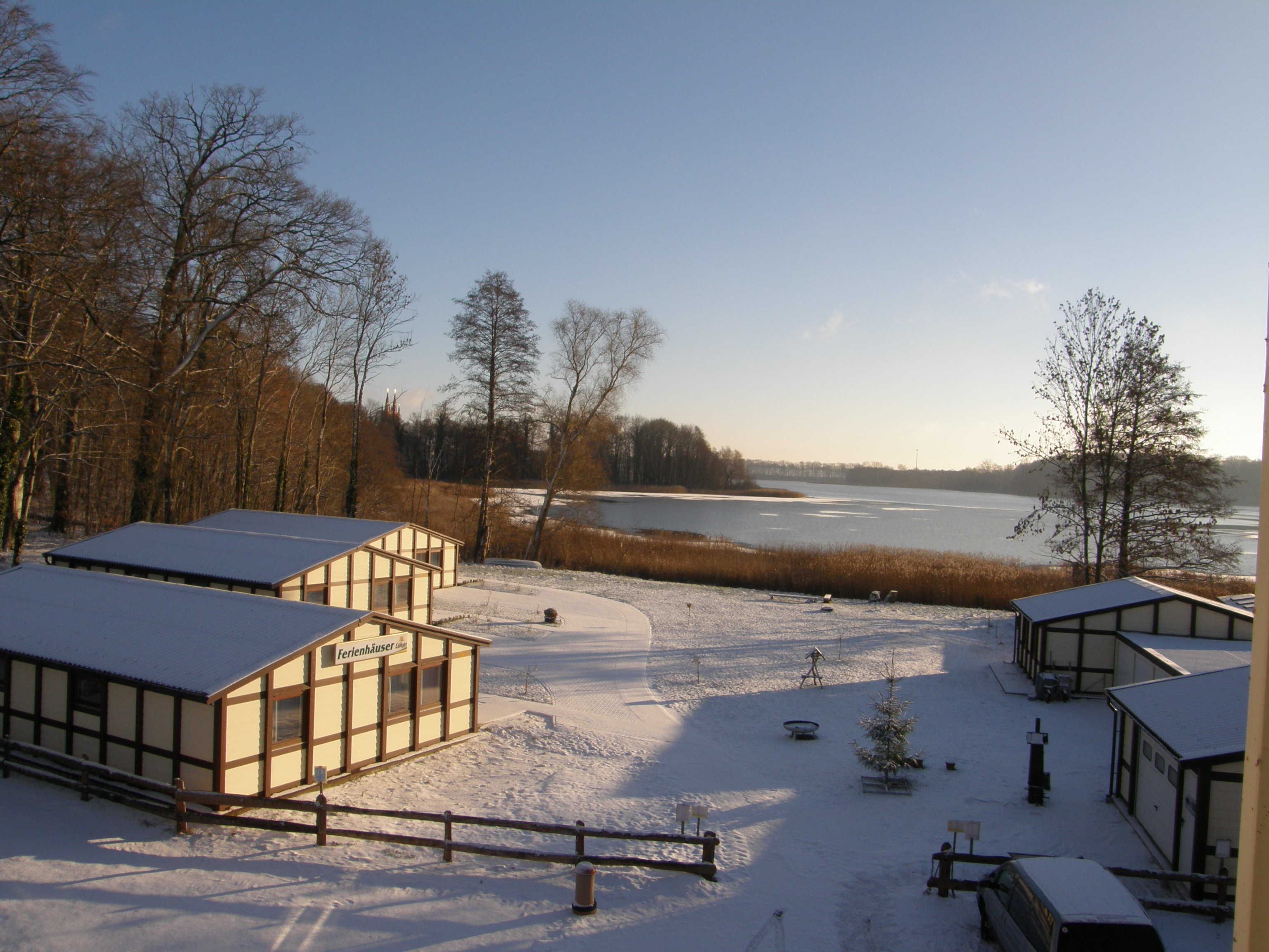 A snow-covered outdoor area with buildings, a lake, and trees.