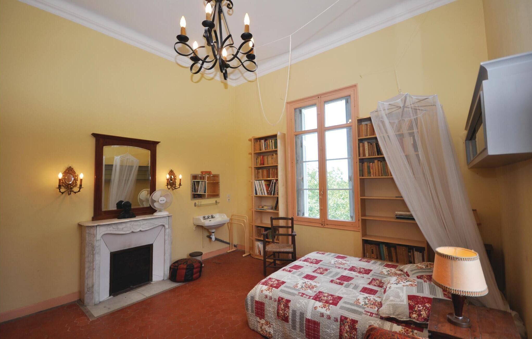 Een slaapkamer met een open haard, een groot raam met uitzicht, een boekenkast en een bed met hemelbed.
