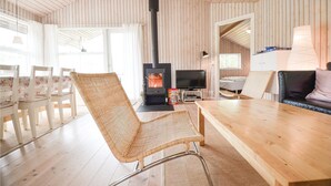 Ein gemütliches Blockhaus-Interieur mit Holzausstattung, Kamin, Fernseher und Essbereich mit Stühlen.