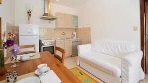 A compact kitchen with a stove, oven, and dishwasher, a dining table with chairs, and a white sofa. - Holiday apartment with terrace and air conditioning (Pula)