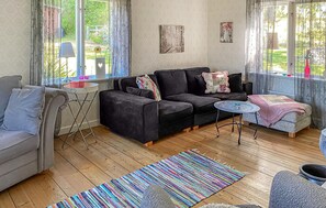 A cozy living room with a sofa, a small table, a colorful rug, and a window with curtains.