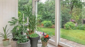 Ein Wintergarten mit großen Fenstern, Topfpflanzen und Blick auf einen üppigen Garten.