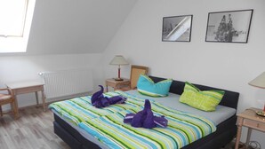 Un dormitorio con cama, escritorio, silla, radiador, lámpara y dos cuadros en la pared.