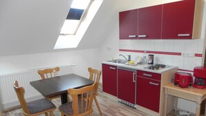 Cocina compacta con una mesa de comedor y sillas, armarios rojos y un tragaluz.