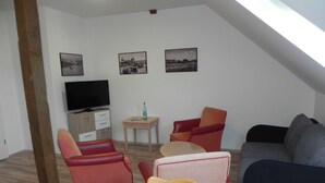 Una sala de estar acogedora con un televisor, una mesita con una botella y tres sillones.