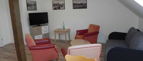 A cozy living room with a TV, a small table with a bottle, and three chairs.