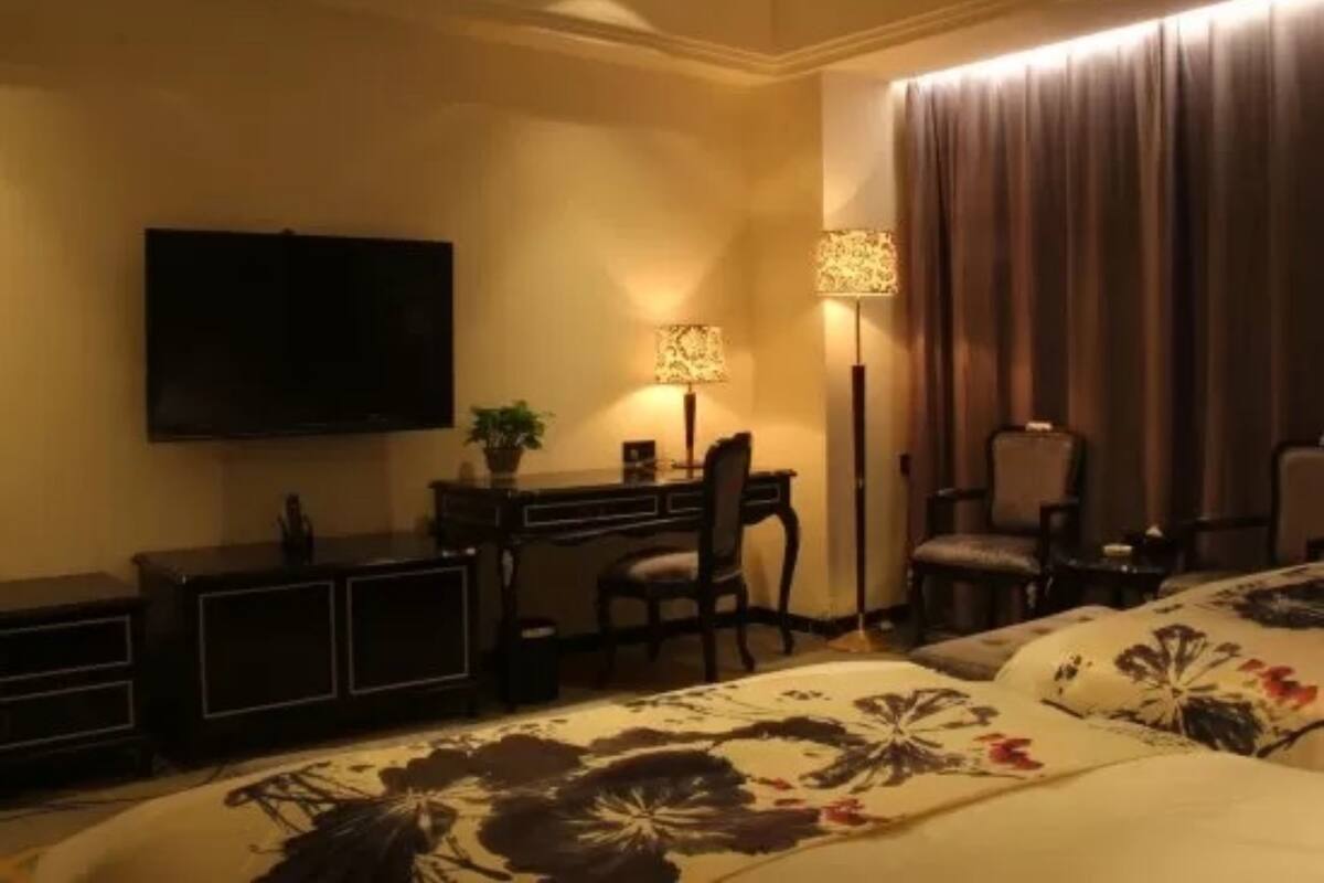 A hotel room with a bed, a desk, a chair, a television, and a lamp.