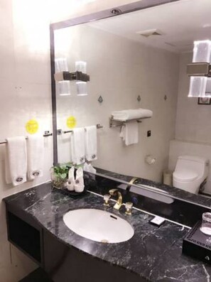 A bathroom with a large mirror, a sink with a gold faucet, and white towels hanging on the wall.