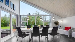 Un'elegante zona pranzo con un tavolo grande, sedie nere e vista su un giardino attraverso ampie finestre.