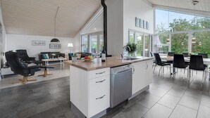 Una cucina moderna con lavastoviglie, una zona pranzo con tavolo e sedie, e un soggiorno con divano e tavolino.