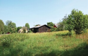 Un bâtiment rustique en bois, doté d’un toit en pente, entouré d’une végétation luxuriante et d’arbres.