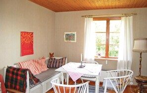 Une pièce chaleureuse avec un canapé, une table à manger et des chaises. Il y a une fenêtre avec des rideaux, une lampe et un tableau au mur.