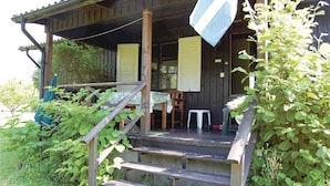 A wooden porch with a table and chairs, surrounded by greenery. - 2 bedroom cozy home in Hamneda (Hamneda)