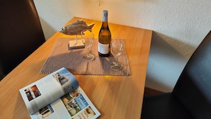 A wooden table with a bottle of wine, two glasses, a wooden fish sculpture, and a magazine on a placemat. - 101 2-room Spülm. (LTO,MNC)(BC.n8) - BUE - Haus Leißner (Büsum)