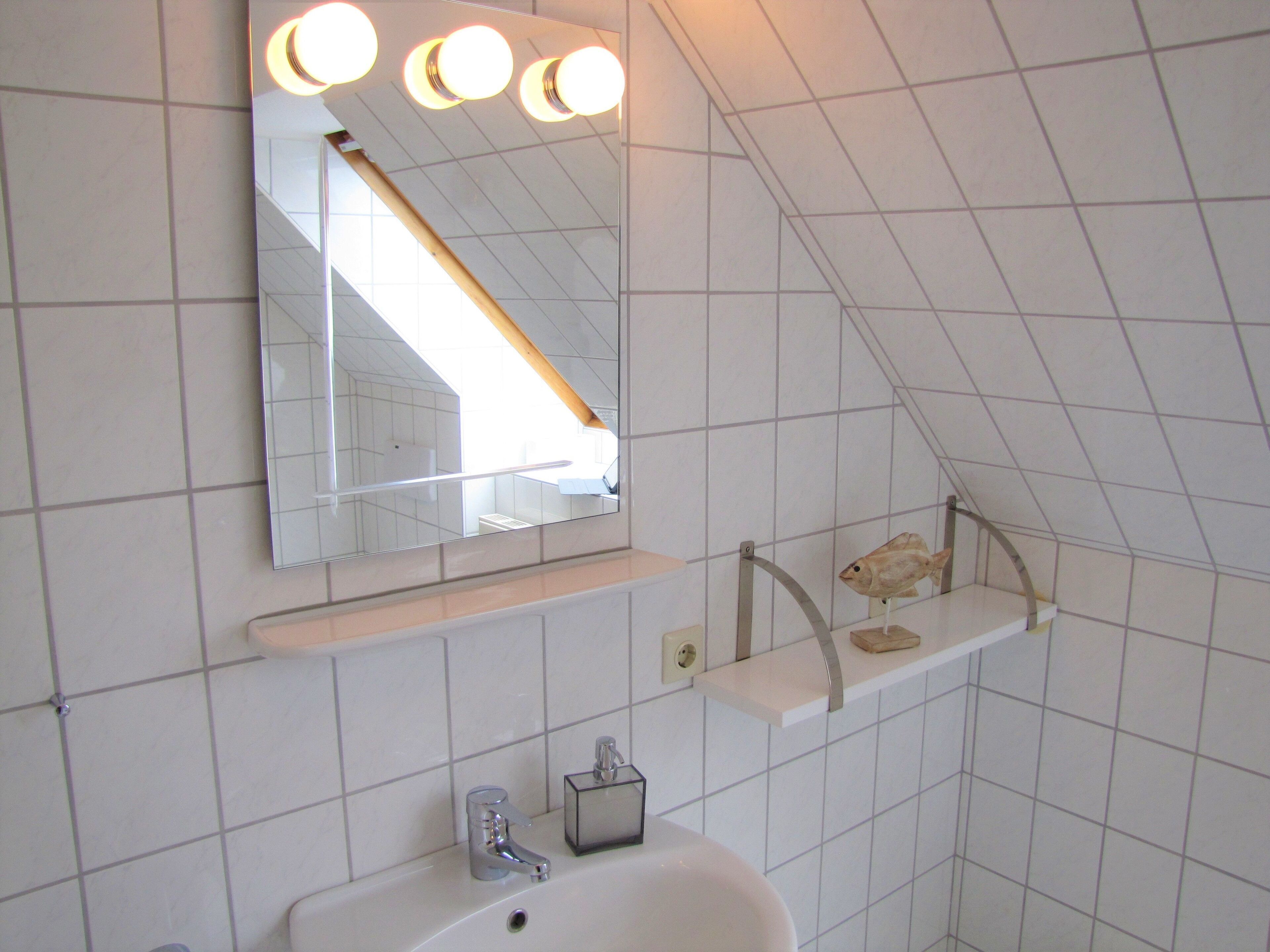 Un bagno con un lavandino bianco, uno specchio illuminato e una decorazione a forma di pesce.