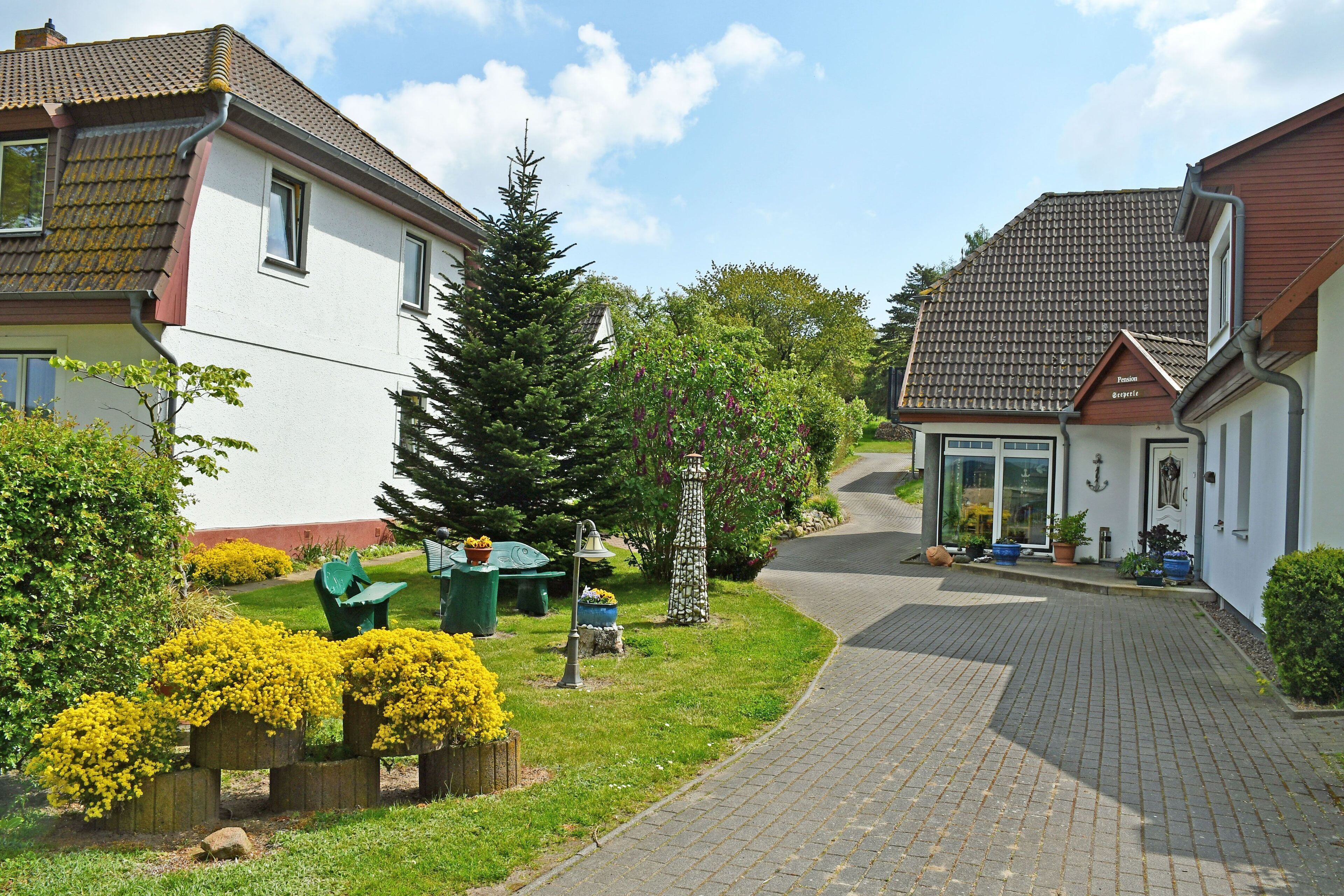 Een woonstraat met twee huizen, een verharde oprit en goed onderhouden tuinen.