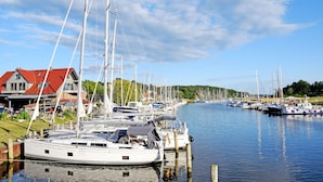 A marina with multiple sailboats docked, a house with a red roof, and calm water reflecting the boats. - Double Room (11) - DEB 006 Pension Seeperle (Sellin)