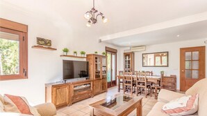 Un salon spacieux équipé d’un téléviseur, de meubles en bois, d’un coin repas avec une table et des chaises, et d’un canapé.