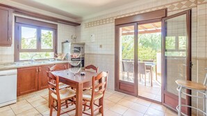 Une cuisine avec une table et des chaises, un four encastré, et une vue sur une terrasse extérieure, accessible par une porte vitrée.