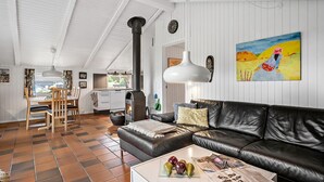 A spacious living room with a black leather sofa, a dining area with a wooden table and chairs, and a kitchen with white cabinets and a stove.