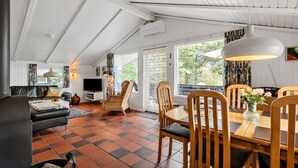A spacious living area with a high ceiling, a dining table with chairs, a sofa, and a television.