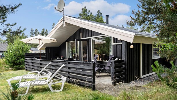 A cabin with a sloped roof, large windows, and a deck area with outdoor seating.