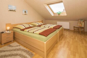 Quarto com claraboia, cama de madeira, mesa de cabeceira, cadeira e radiador.